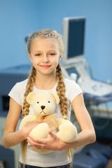 The girl with a soft toy in the hospital on a background of ultrasound machines, smiling and playing