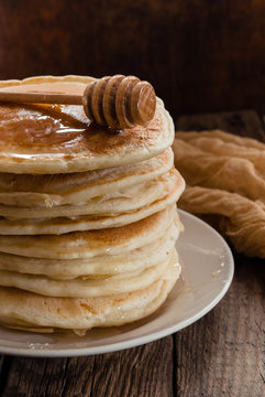 Stack of pancakes with honey on wooden background.