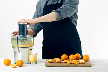 Anonymous man wearing an apron, preparing healthy orange juice, using modern electric juicer,...
