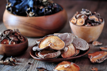 Various organic dried Chinese mushrooms in a wooden bowl on the old wooden background.