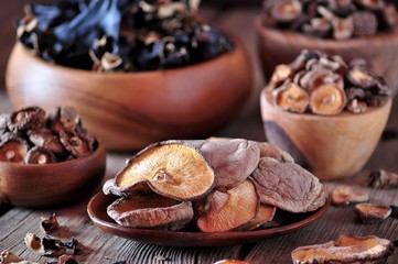 Various organic dried Chinese mushrooms in a wooden bowl on the old wooden background.