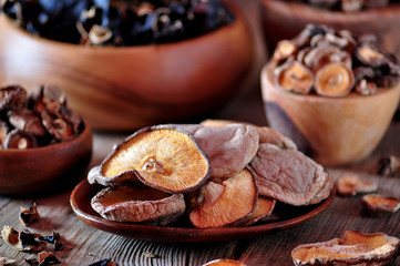 Various organic dried Chinese mushrooms in a wooden bowl on the old wooden background.