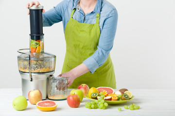Anonymous woman wearing an apron, preparing healthy fruit juice using modern electric juicer, healthy lifestyle concept on white background - obrazy, fototapety, plakaty