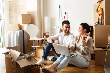 Young couple moving in new home.Sitting on floor and relaxing after unpacking.Looking something on...