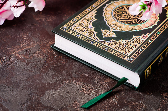 Islamic Book Koran and spring flowers brunch on dark background with arabic calligraphy that means the Holy Quran. Sring concept. Selective focus