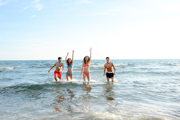 four happy friends young people man and woman having fun at ocean beach jumping together in the sea