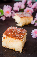 Basbousa (namoora or revane) - semolina cake on dark background with spring flowers. Selective focus