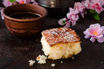 Basbousa (namoora or revane) - semolina cake on dark background with spring flowers. Selective focus