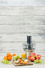 Modern electric juicer, various fruit and glass of freshly made juice, healthy lifestyle concept