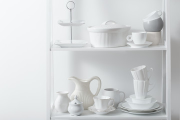 Clean dishes and vases on white wooden shelf