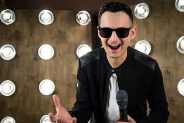 Male singer in sunglasses performing on scene in projectors lights
