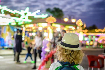 Fototapeta premium Back view of joyful cute child boy on night bokeh amuzement park outdoors background