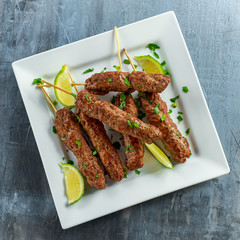 Homemade Kofta kebabs on skewers with lime and parsley on white plate