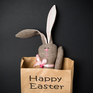 Easter bunny in a paper bag. Rabbit. Black background. Easter ideas. Easter eggs. Space for text. Black lettering happy easter.