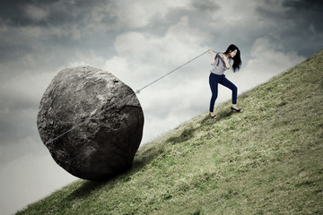 Businesswoman pulling stone on the hill - obrazy, fototapety, plakaty