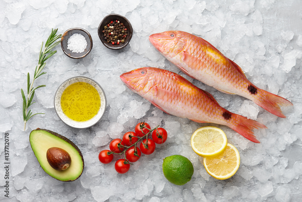 Poster fresh red mullet fish with lemon, rosemary, avocado, chili pepper and spices on icy stone background