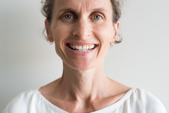 Close up of middle aged woman with grey hair and cream top smiling (cropped and selective focus)