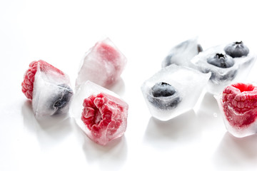 Icecubes with frozen berries on white background