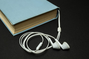 Old blue book, and white headphones on a black background