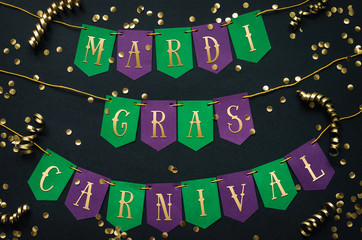 Mardi Gras carnival yellow lettering on paper handmade green and purple festive garland, black background. Holiday decoration postcard, greeting, invitation card, banner. © mykolastock