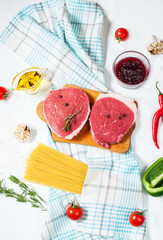 Raw beef steak with pasta, tomatoes, mushrooms and cheese on white table background, top view