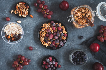 Breakfast with muesli, fruits, frozen berries, nuts on dark background. Healthy food concept. Flat lay, top view
