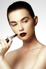 Fototapeta premium Fashion and beauty. Beautiful young woman with wine lipstick. Brunette model with dark red colored pomade. Beautiful model girl applying lipstick