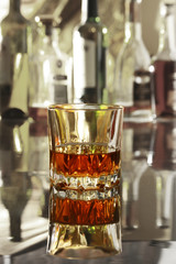 Glass of cognac, brandy or whiscy on mirror table. bottles in a bar on the background