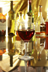 Glass of red wine on mirror table. bottles in a bar on the background