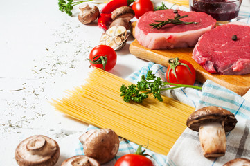 Raw beef steak with pasta, tomatoes, mushrooms and cheese on white table background