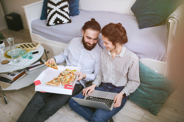 Young hipster male female couple home eating pizza with laptop