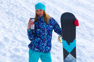 in a cold weather woman holding a snowboard and a thermos of hot tea
