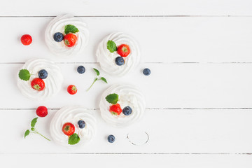 Meringues Pavlova cakes with strawberry and blueberry on wooden white background. Sweet dessert. Flat lay, top view
