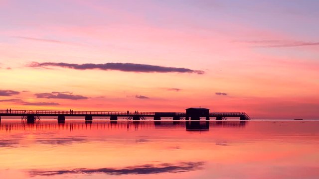 Silhouette of pier at twilight. Beautiful and colorful sunset sky reflected in the sea water, people walking by on the pier