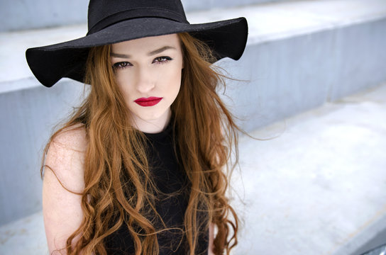Portrait of young stylish redhead woman with hat outdoors