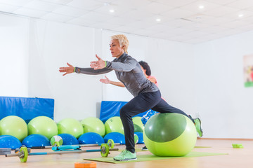 Active middle-aged woman working out with stability ball taking part in group fitness class