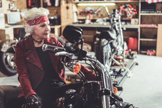 Smiling pensioner sitting on motorcycle in garage
