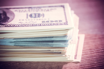 Stack of US dollars in cash in wooden desk.