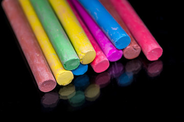 Multi colored chalk isolated on black background .