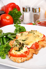 Pork chops with cheese with greens and tomato on white plate decorated with parsley and lettuce on background vegetables