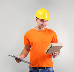 Handsome warehouse worker with clipboard and carton box on light background