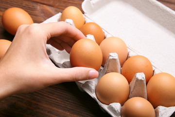 Woman taking raw egg from packaging on wooden background