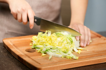 Female hands cutting Chinese cabbage at table in kitchen