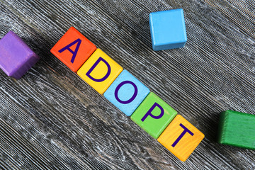 Colorful cubes with word ADOPT on wooden background