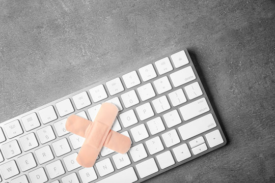 Computer repair concept. Wireless keyboard sealed with plaster, on grey background
