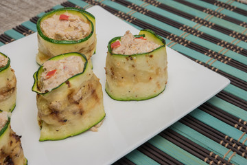 Grilled zucchini rolls with curd cheese and tuna on plate.