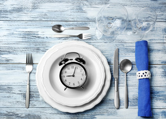 Alarm clock in empty plate on wooden background