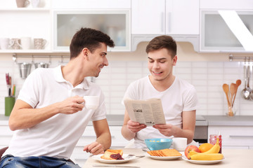 Happy gay couple having breakfast in kitchen