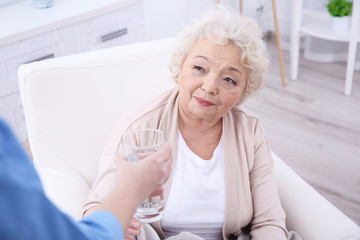 Elderly woman taking glass of water in light room