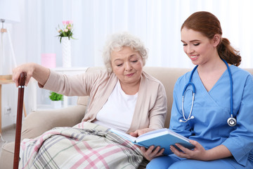 Obraz premium Nurse reading book to elderly woman on couch